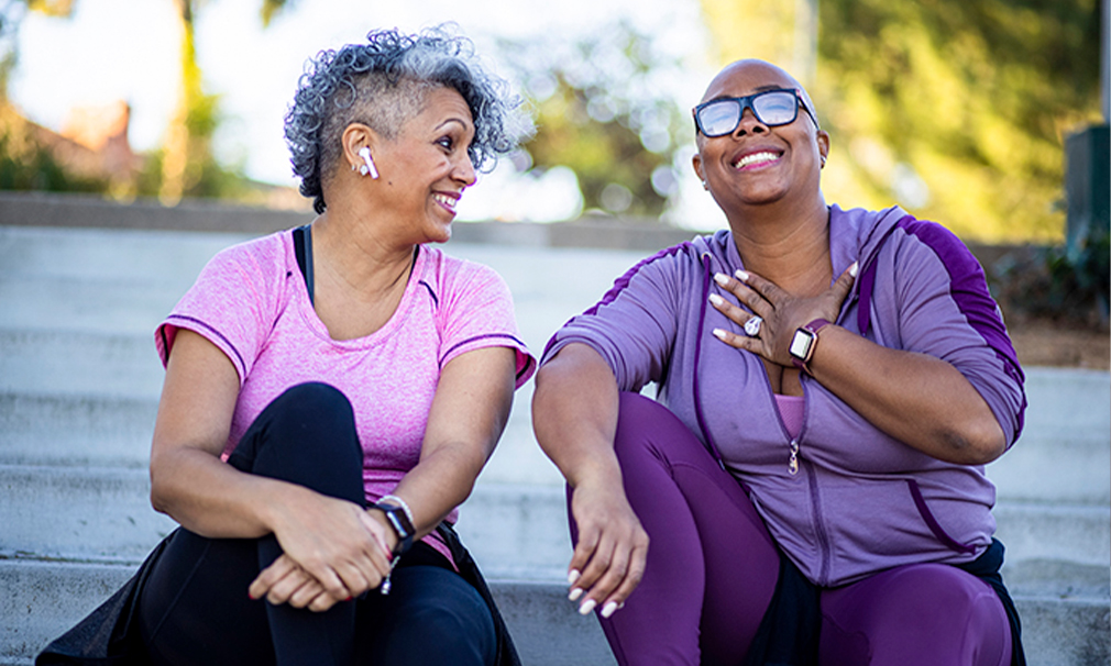 Two individuals sitting down outside wearing purple attire laughing together.