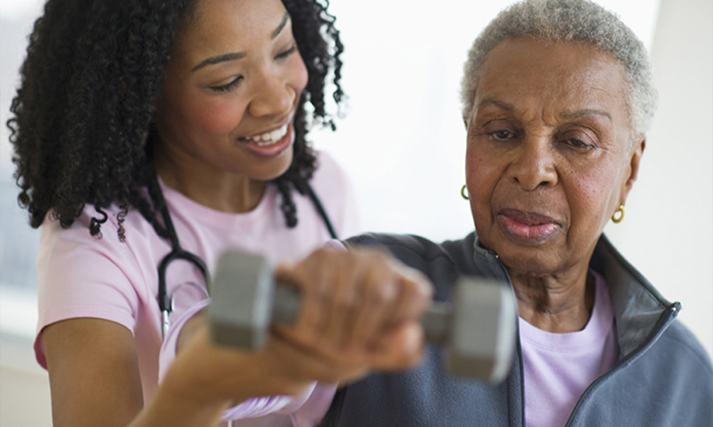 Elderly woman trying to lift a weight as a female nurse helps her.