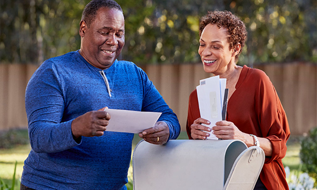 Male and female standing at a mailbox outside reading their mail.